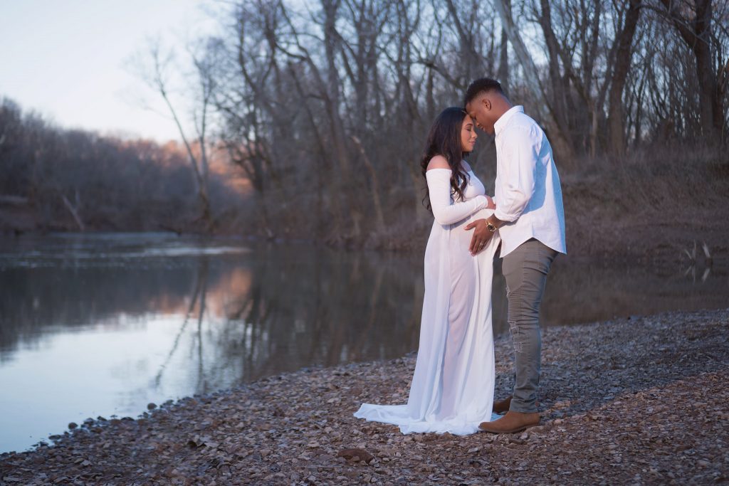 Romantic couple maternity session along the water with blue background white dress in Clarksville, TN