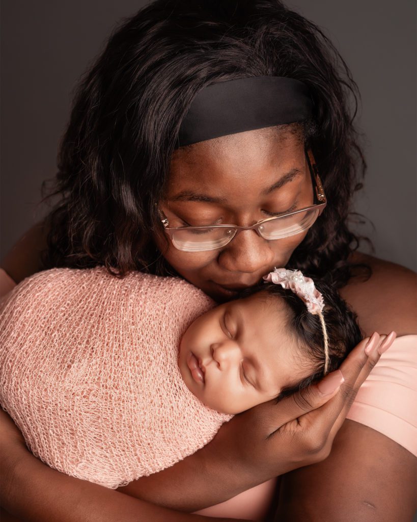 Newborn daughter and mother kissing temple in studio with gray grey backdrop in Clarksville Tennessee tn