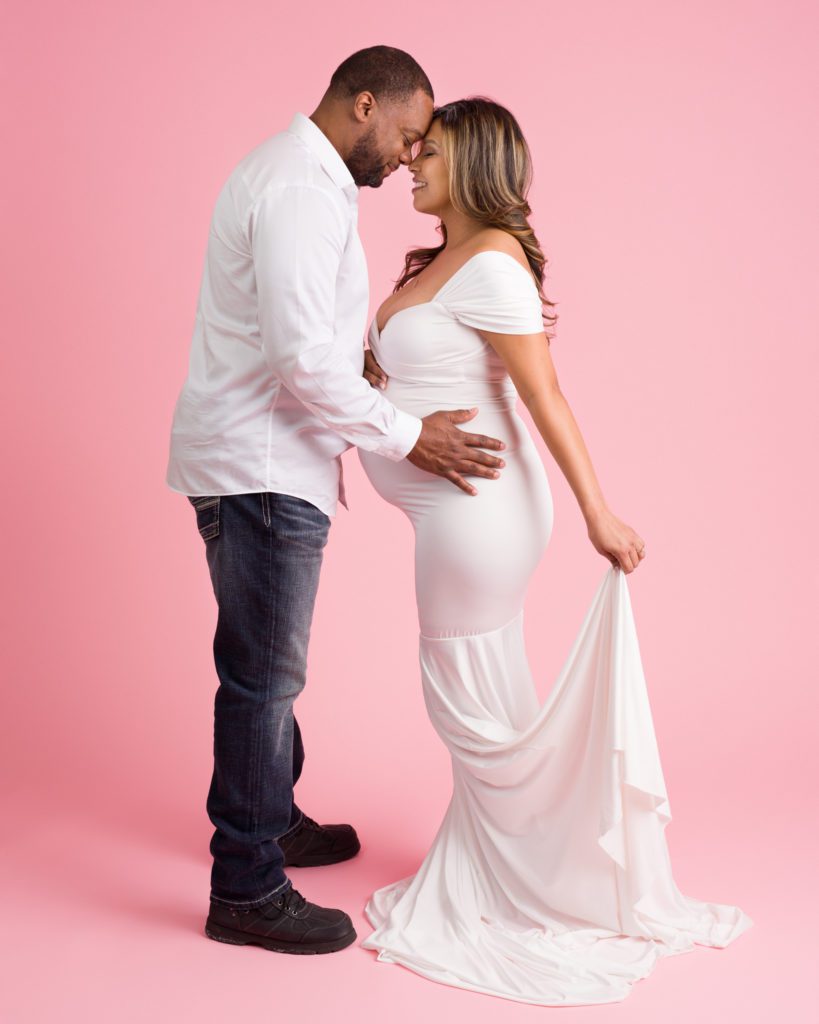 Studio maternity session in white dress with prink backdrop