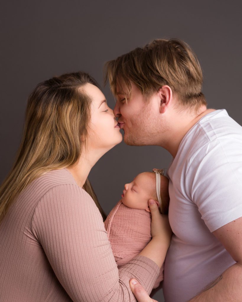 Mom dad and newborn baby in studio kissing