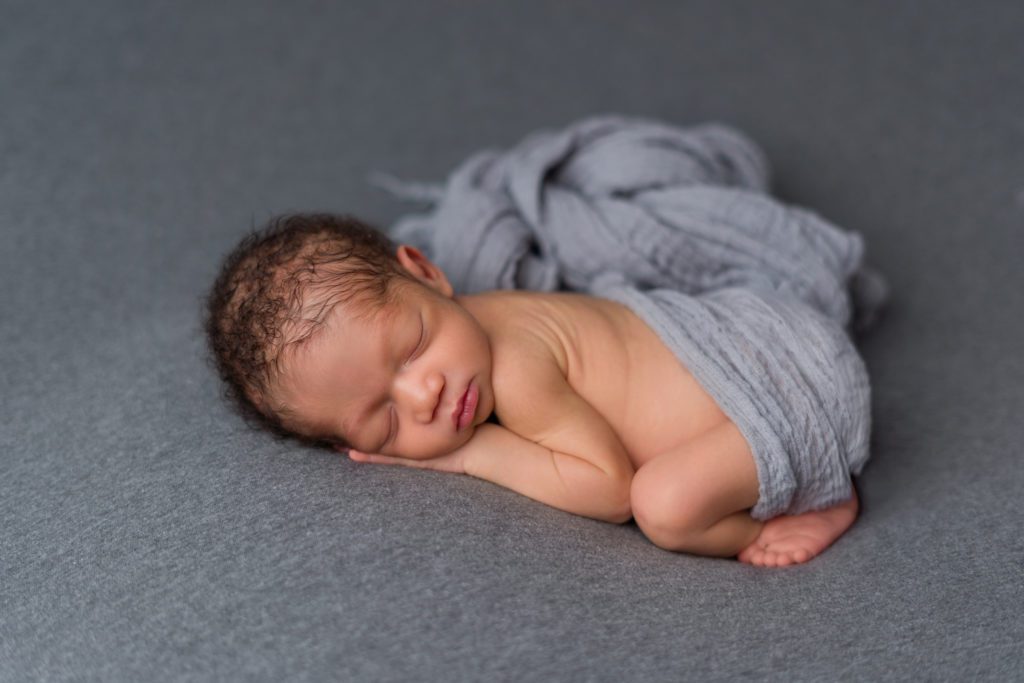 Newborn baby boy sleeping bums up on grey