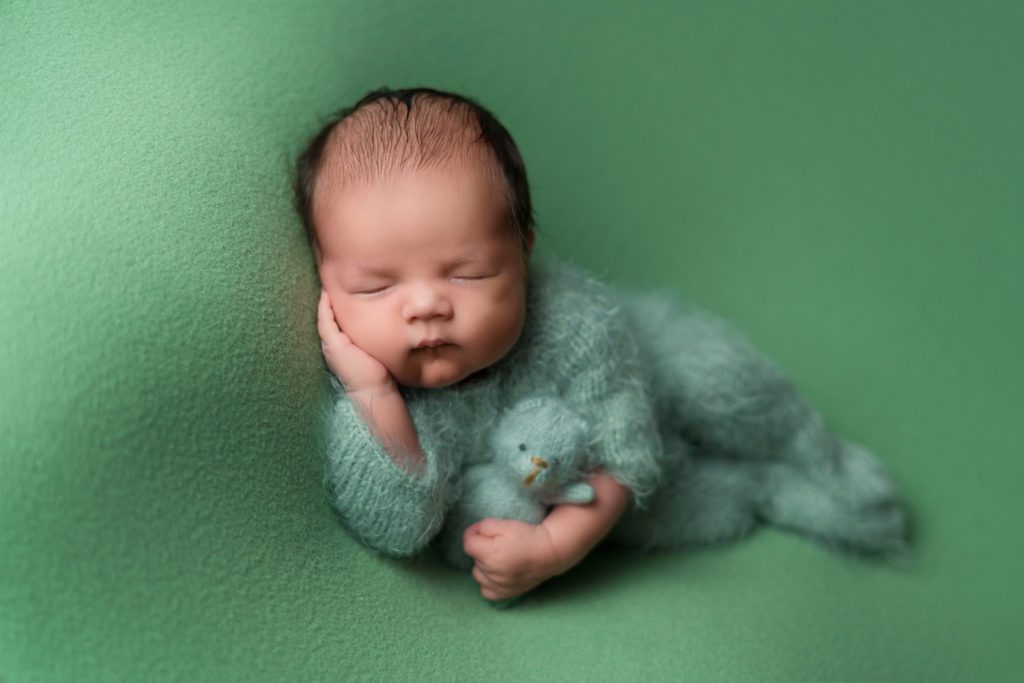 Newborn baby boy sleeping with green teddy bear