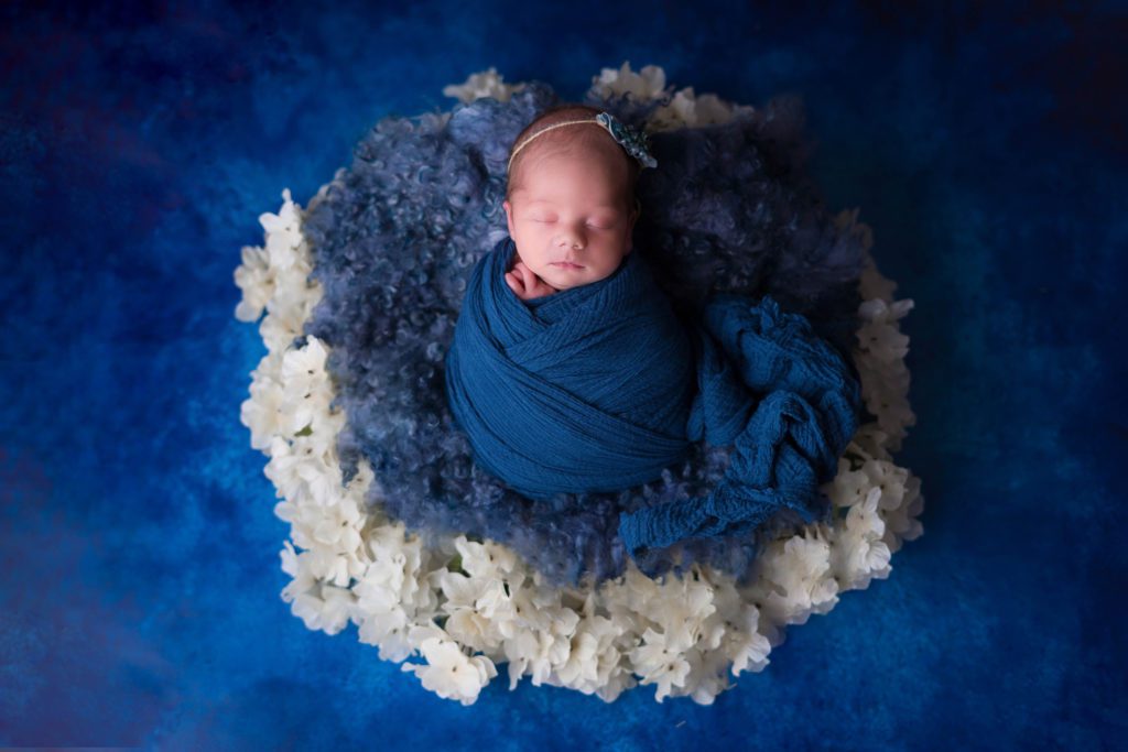 Newborn baby girl with flowers on blue