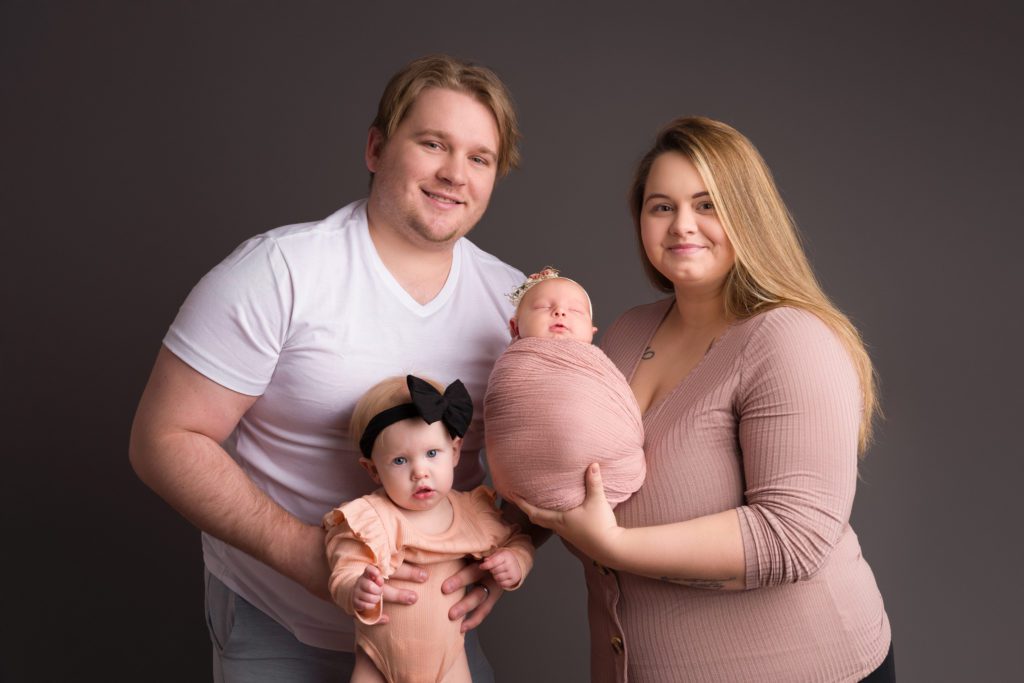 Studio newborn photo of little baby girl in blush pink wrapped up, family of 4 photo with thunder gray backdrop