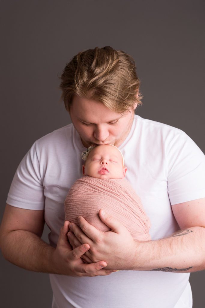 Studio newborn photo of little baby girl in blush pink wrapped up, father daughter photo with thunder gray backdrop