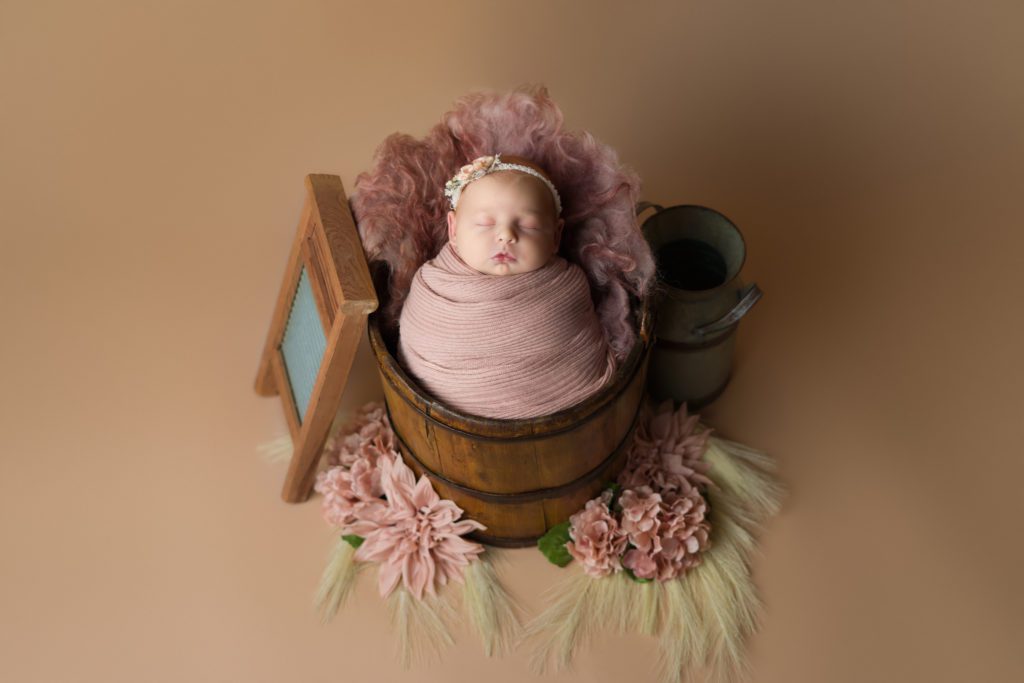 Studio newborn photo of little baby girl in blush pink and wrapped up in a bucket. Pink western theme