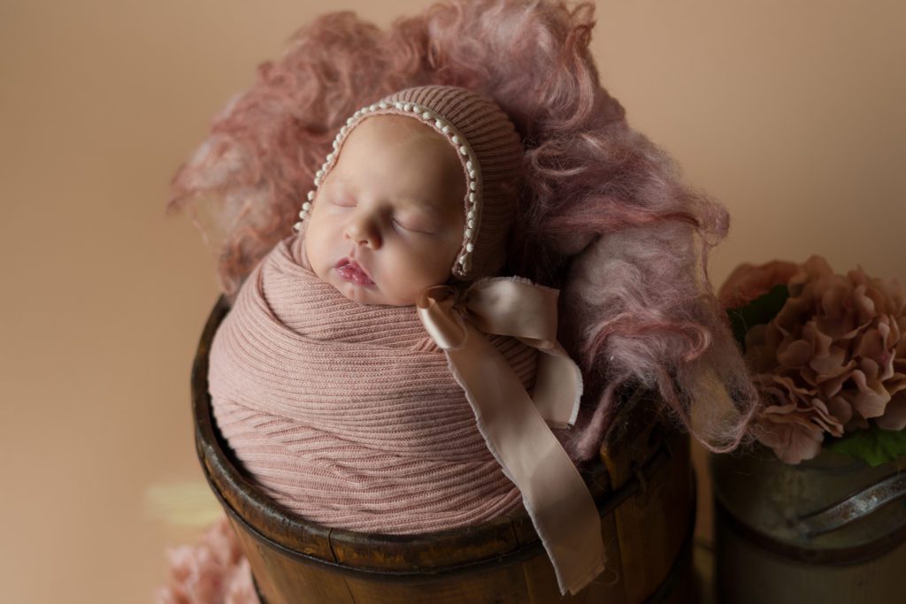 Studio newborn photo of little baby girl in blush pink and wrapped up in a bucket