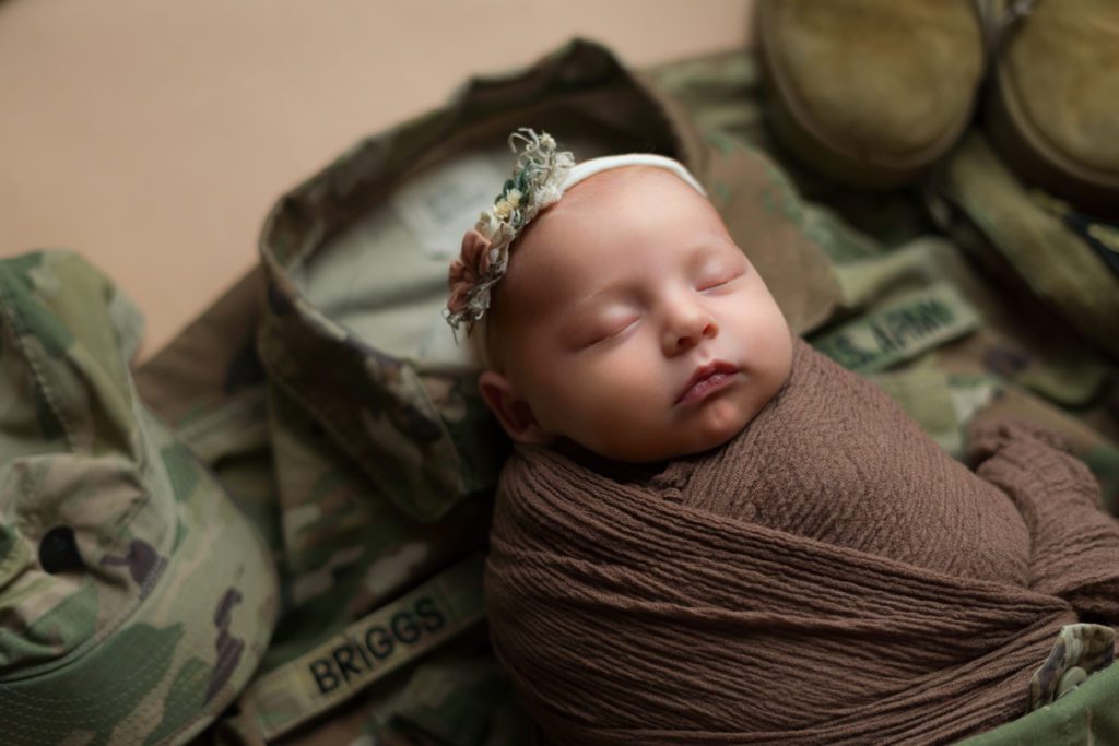 Studio newborn photo of little baby girl in neutral brown and wrapped up with military US Army uniform and boots