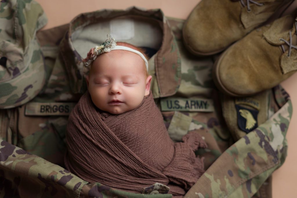 Studio newborn photo of little baby girl in neutral brown and wrapped up with military US Army uniform and boots