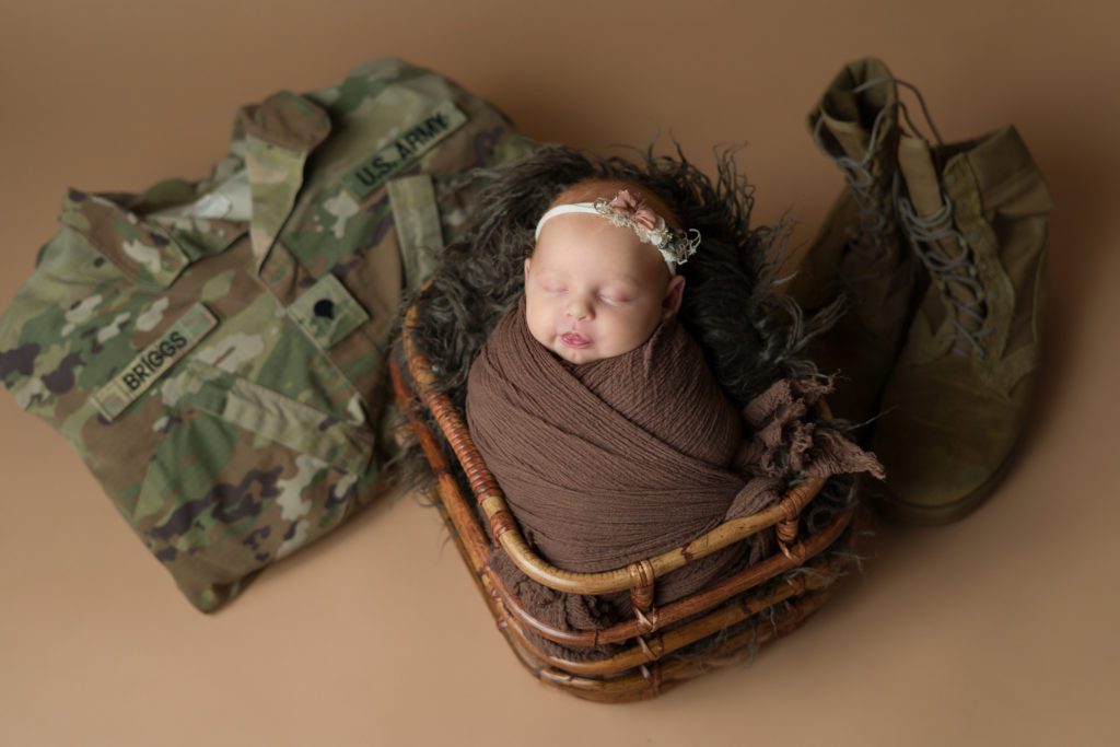 Studio newborn photo of little baby girl in neutral brown and wrapped up with military US Army uniform and boots