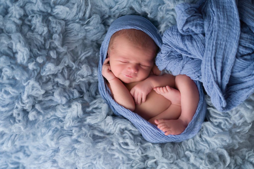 Studio posed newborn with blue fur smiling in womb pose