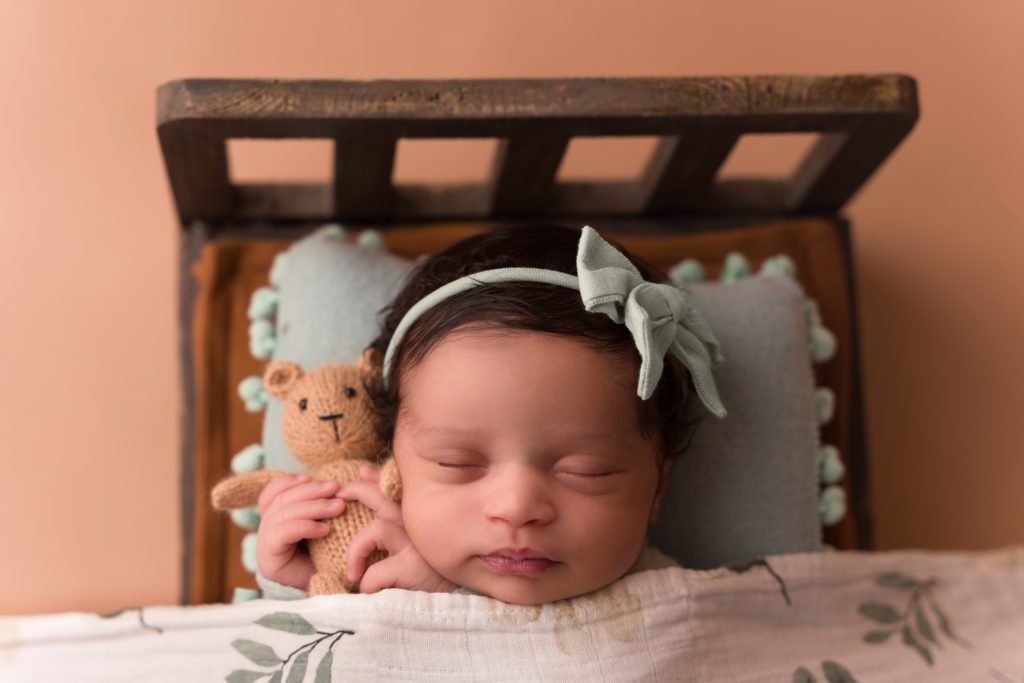 Studio posed newborn baby with with sage green in bed.